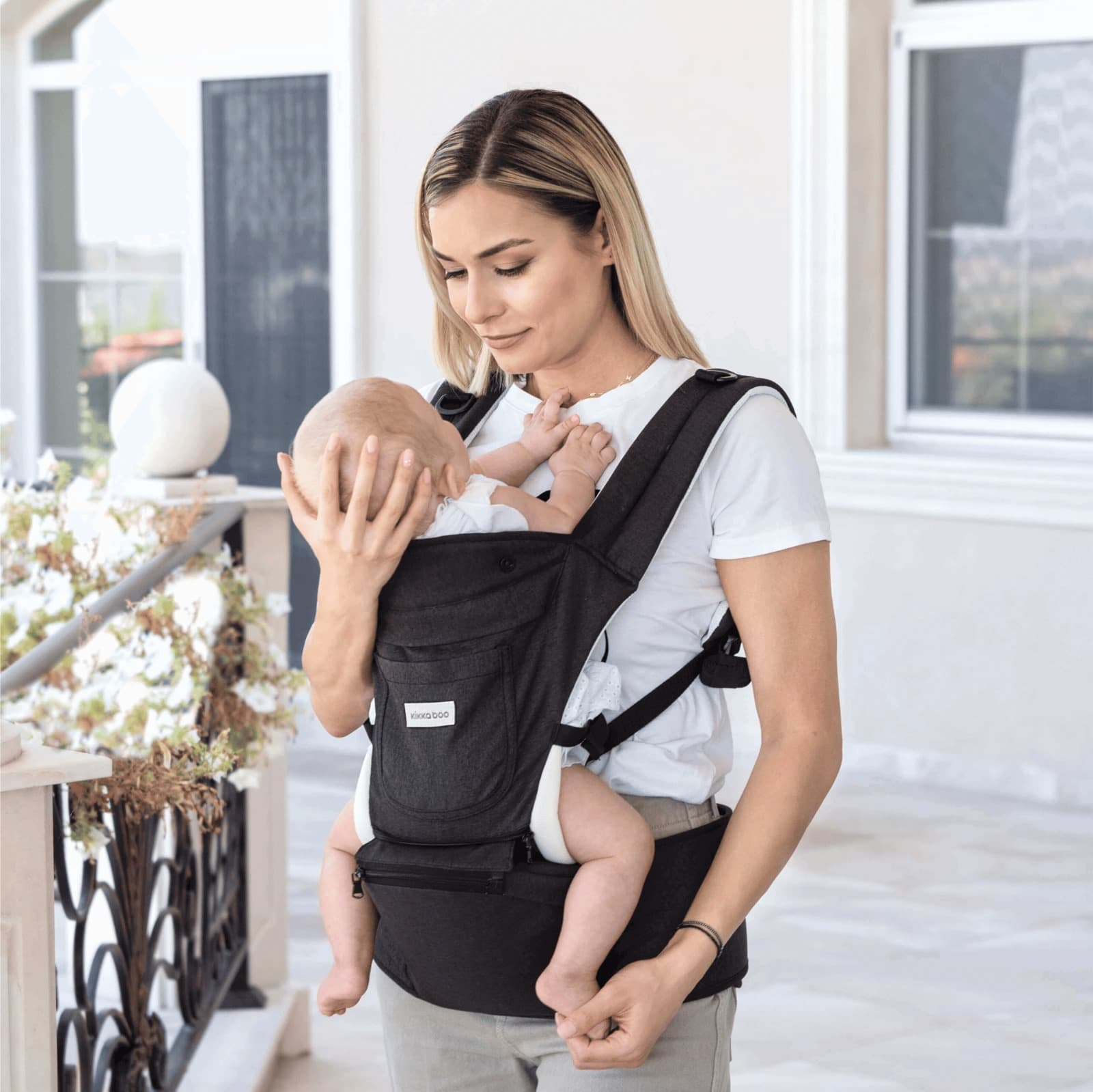אמא מחזיקה תינוק במנשא Chloe אפור, פונה החוצה, בחצר.
